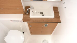 A compact bathroom with a white sink, a wooden cabinet, and a toilet. - Sun-Kissed Sailing Adventure in Istria, Croatia (Pula)