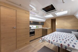 Eine kompakte Küche mit Einbaugeräten, ein Essbereich mit Tisch und ein Bett mit gemustertem Überwurf.