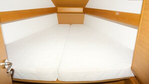 Habitació compacta amb un llit individual, un capçal de fusta, un petit espai d'emmagatzematge a la part superior i una porta amb un pom d'alumini.