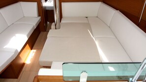 L'intérieur d'un bateau, avec un banc rembourré de coussins blancs, une table en verre et un plancher en bois.