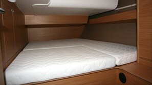 Ein schmaler, holzgetäfelter Innenraum mit einem Einzelbett, eingebauten Stauraum und einem kleinen Hängeschrank.