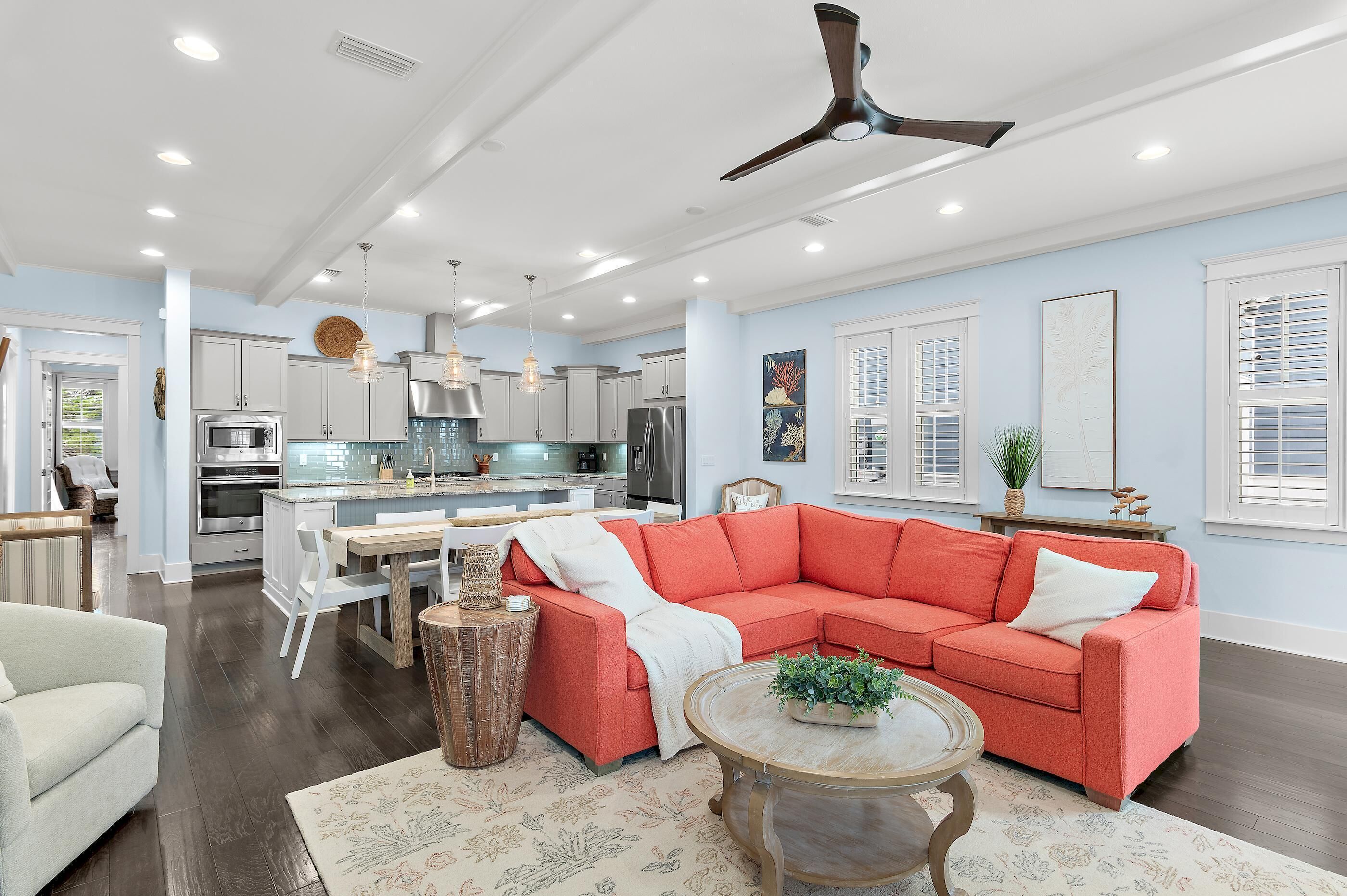 A spacious living room with a red sectional sofa, a round coffee table, and a dining area with a white table and chairs.