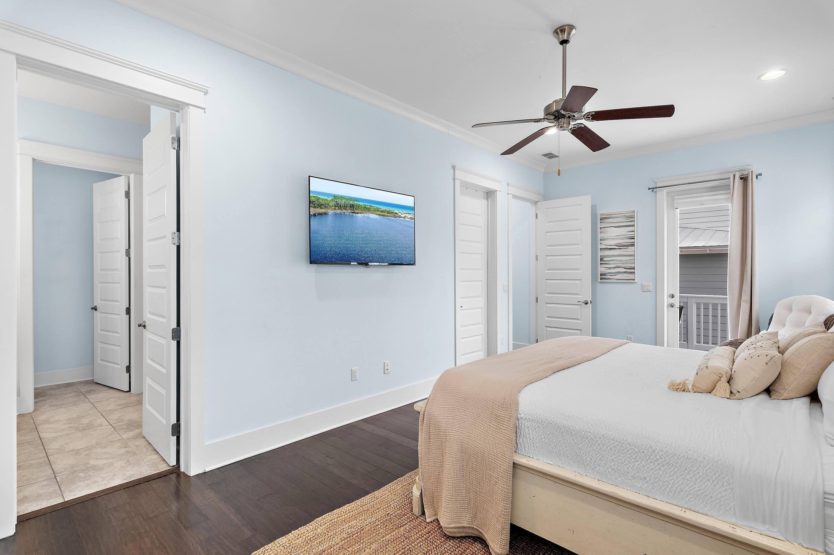 A bedroom with a bed, a ceiling fan, a TV, and a view of a body of water through a window.