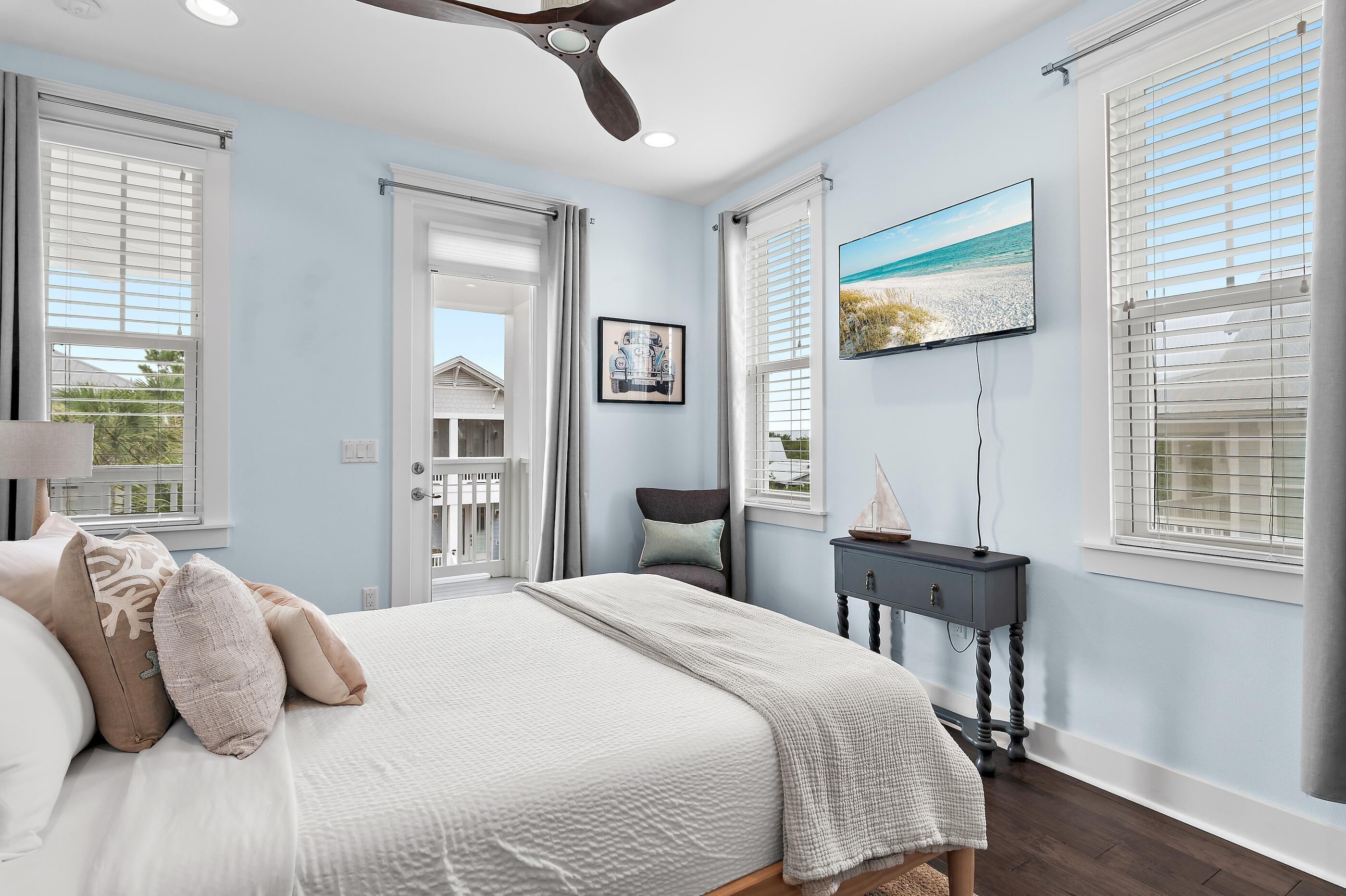 Une chambre à coucher avec un lit, un ventilateur de plafond, un bureau et une fenêtre avec des stores.