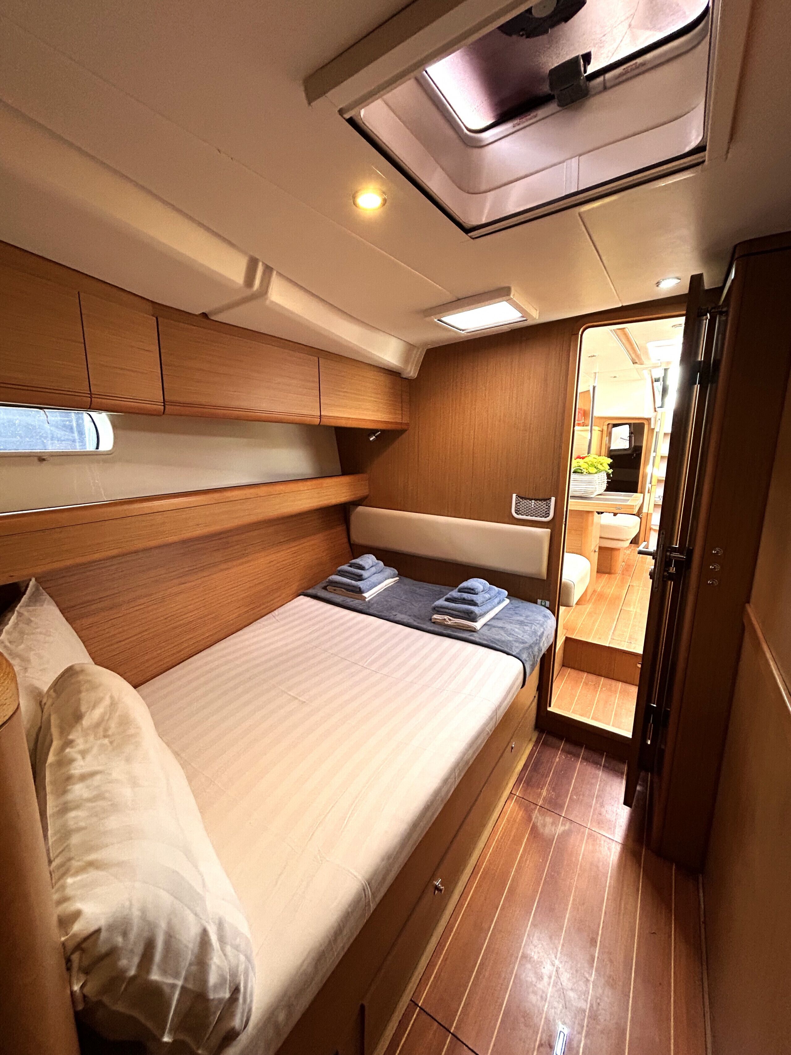 A compact interior with a bed, wooden cabinets, a skylight, and a small kitchenette.