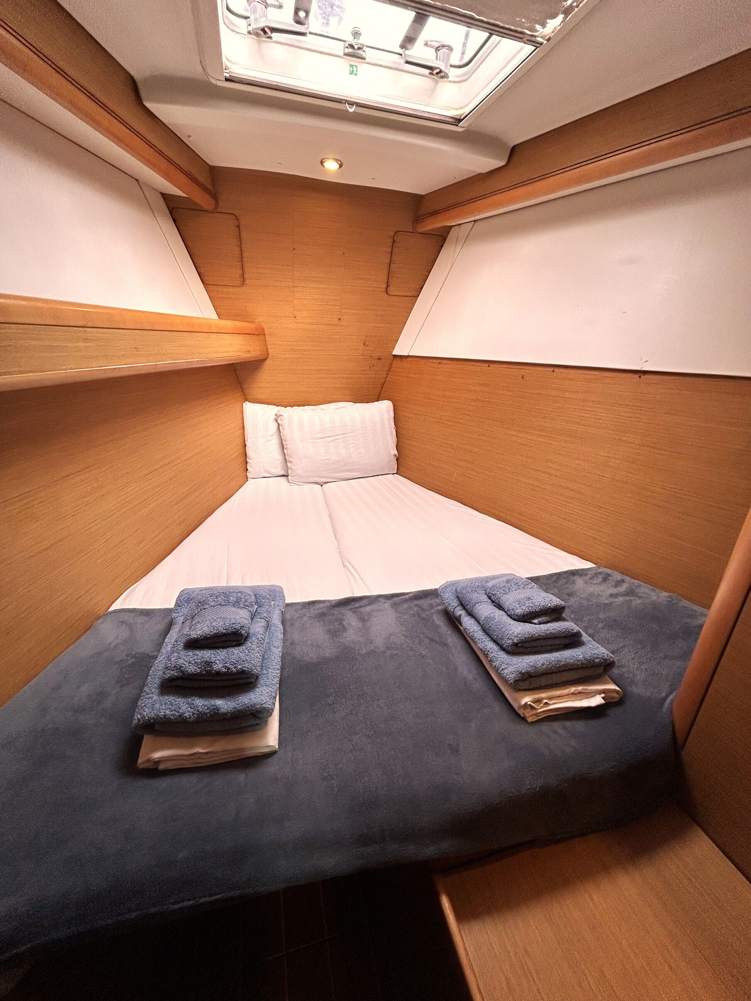 Una cabaña estrecha con una cama individual, paredes de madera y un tragaluz.