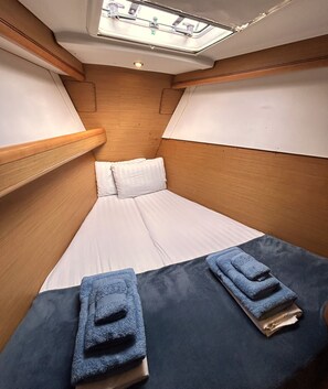 A compact cabin with a single bed, wooden headboard, and a skylight.