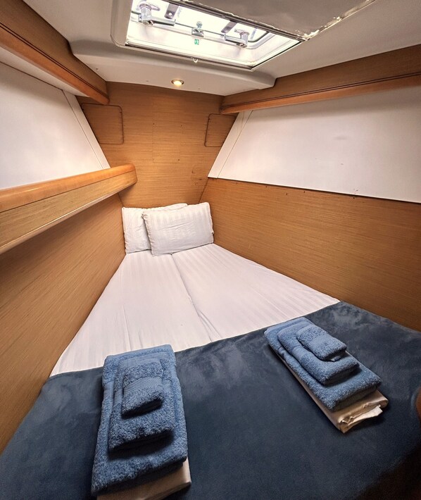 A compact cabin with a single bed, wooden headboard, and a skylight.