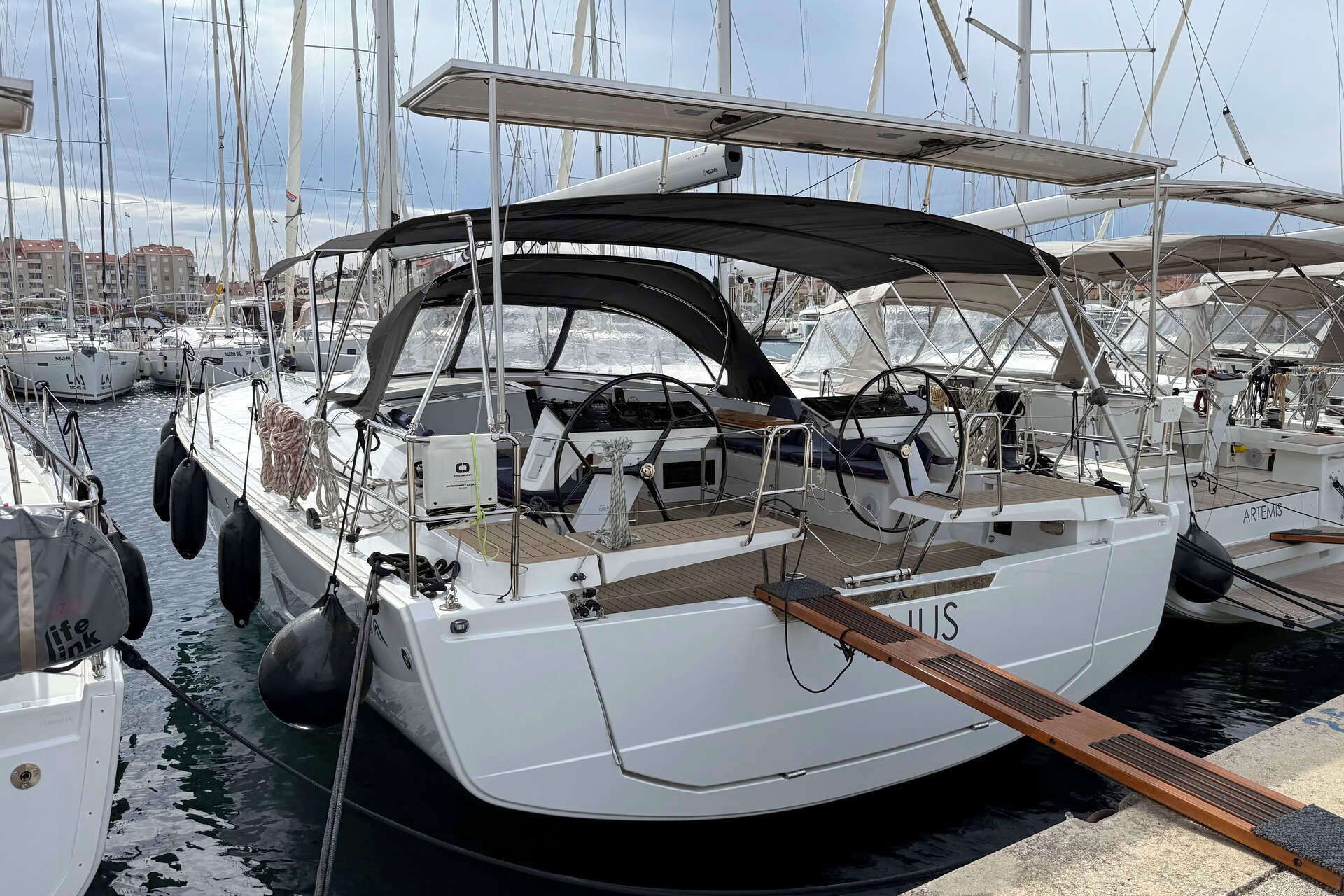 A marina with multiple sailboats docked, featuring white hulls, black canopies, and a wooden deck.