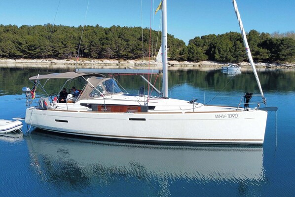 Un velero amarrado en un puerto deportivo con una orilla boscosa al fondo.