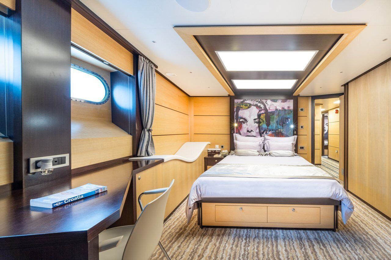A modern hotel room with a bed, desk, chair, and a large window.