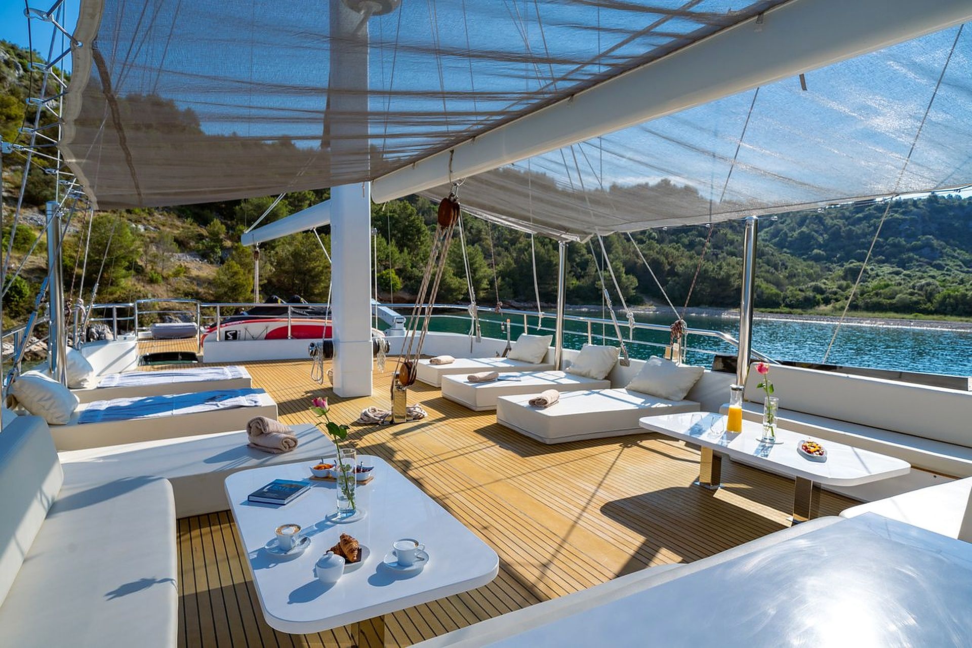 A sunlit deck with seating and tables, overlooking a body of water and greenery.