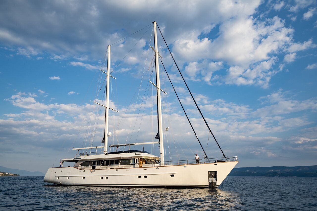 A large yacht with multiple decks, a cabin with windows, and a person standing on the deck.