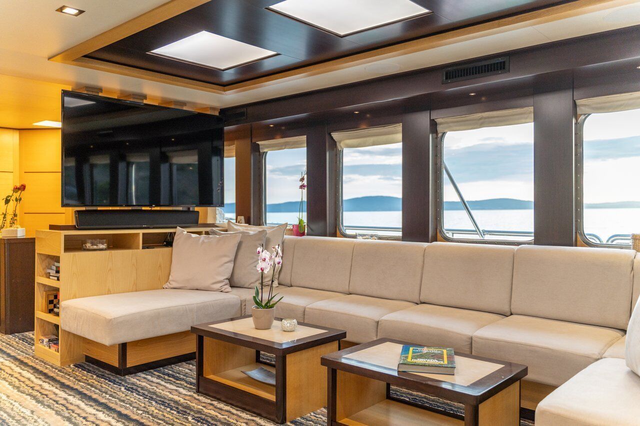 A modern living room with a sofa, coffee table, TV, and large windows offering a view of the water.