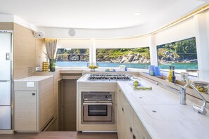A compact kitchen with a gas stove, oven, and a view of the sea.