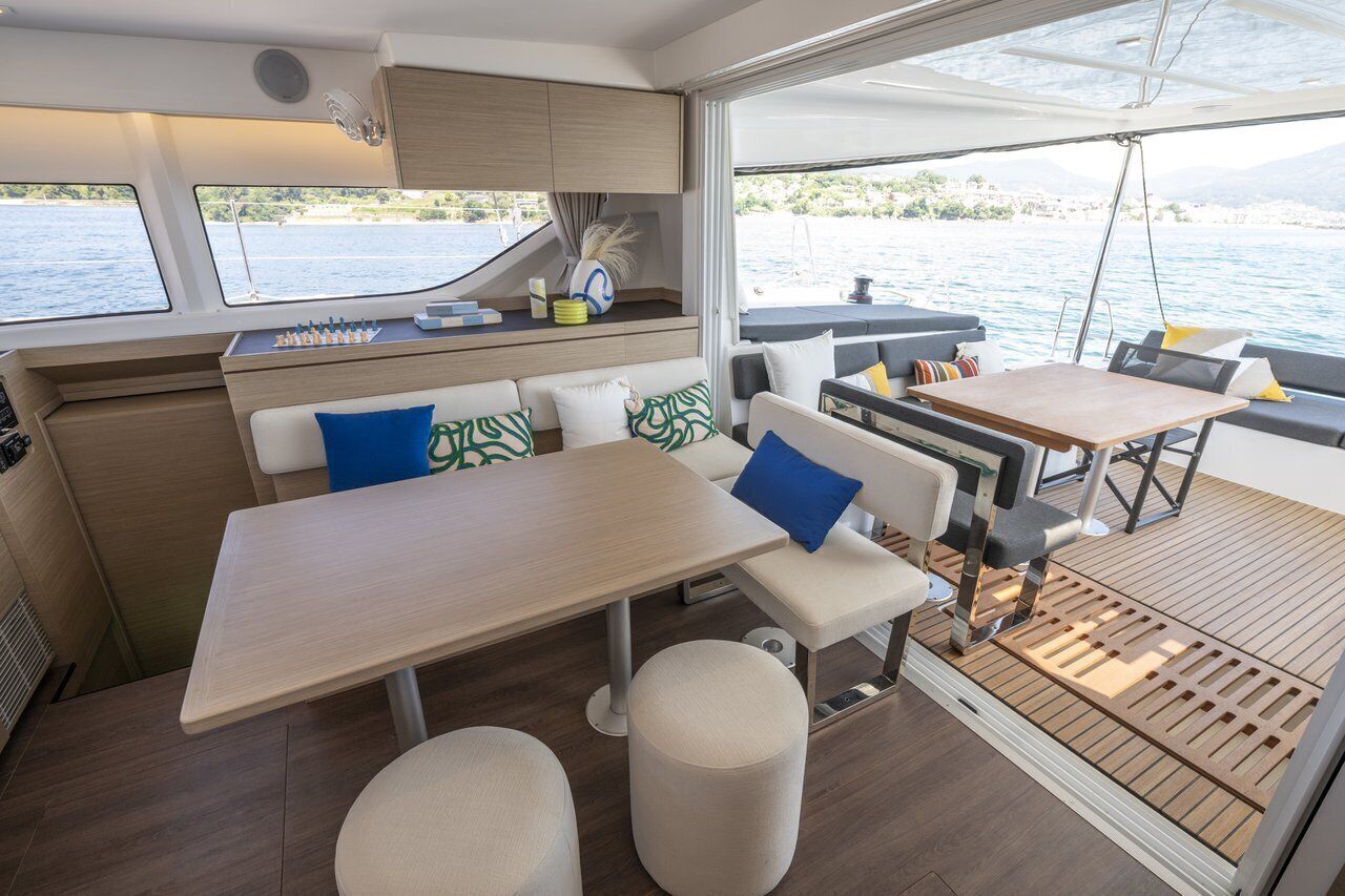A yacht interior with a dining area, seating, and a view of the water.