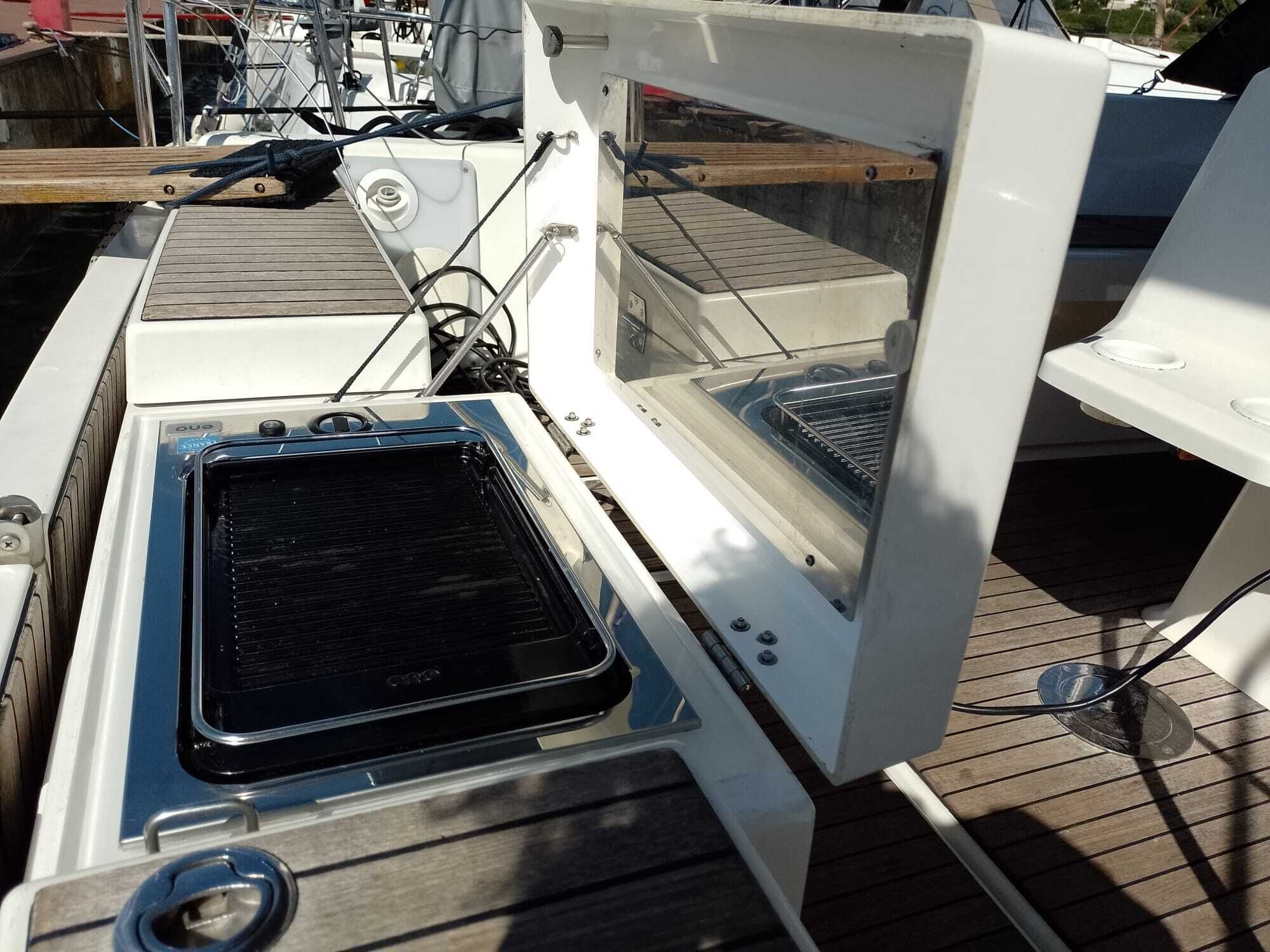 Convés de barco com churrasqueira, uma estrutura branca com janela e corrimão de metal.