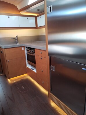 A compact kitchen with a stainless steel refrigerator, wooden cabinets, and a built-in oven. - Sun-Kissed Sailing Adventure in Northern Croatia (Punat)