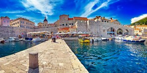 A historic waterfront with stone buildings, a dock with boats, and a paved walkway. - Dubrovnik Delight: A Sun-Kissed Sailing Experience (Komolac)