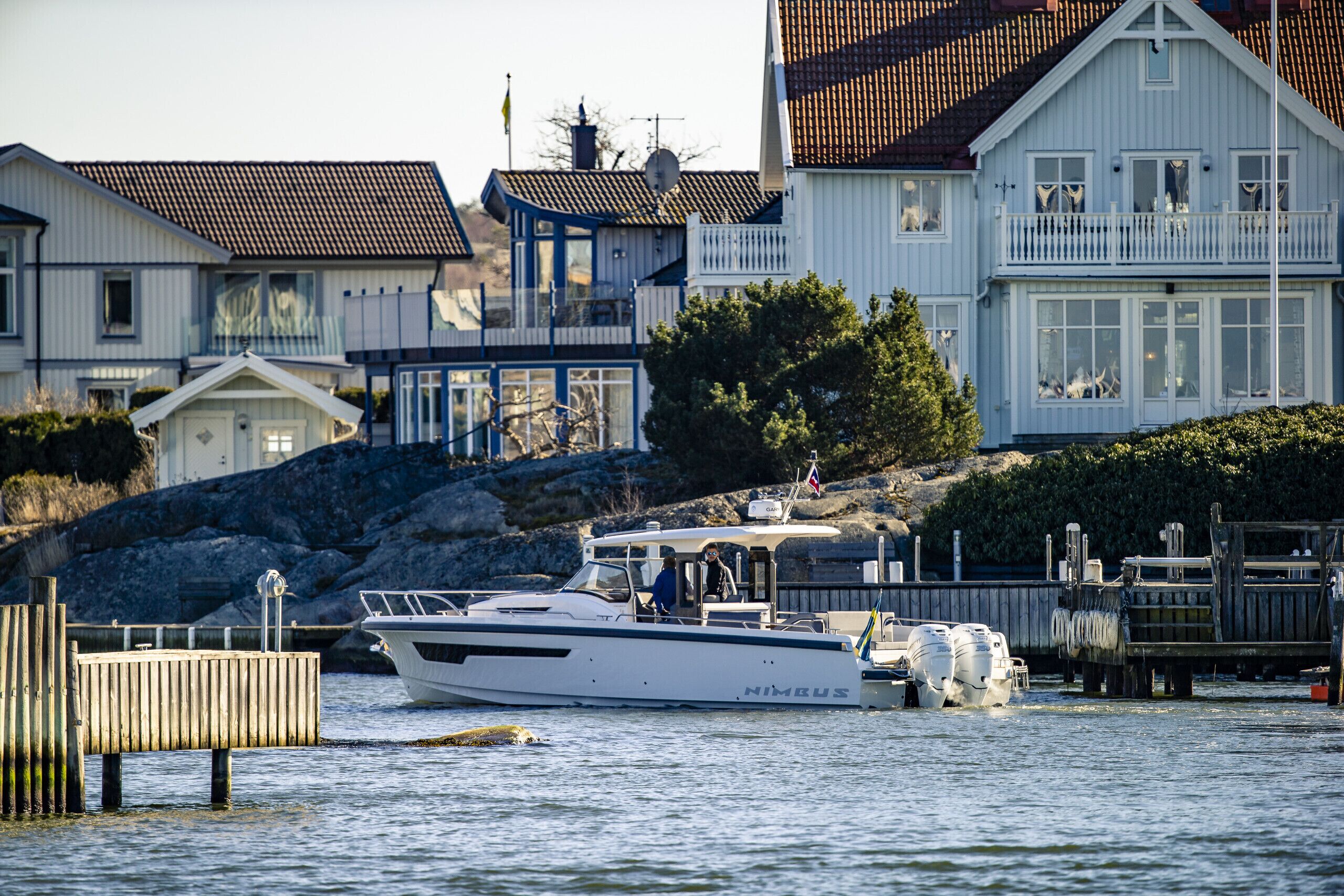 A white boat docked at a pier with a house in the background.
