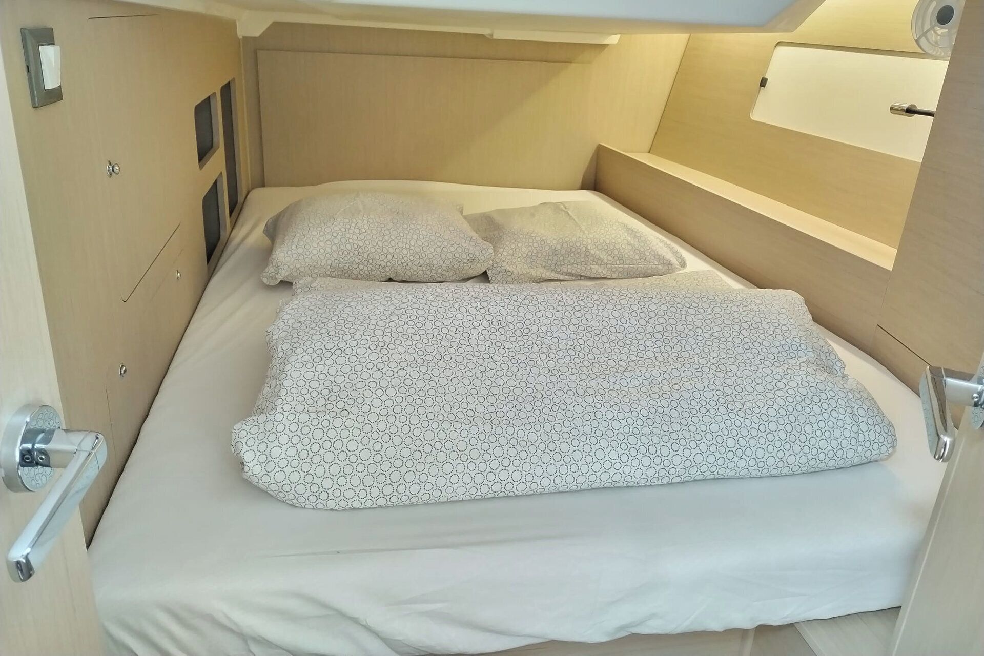 Un llit compacte amb un llençol estampat, un reposacapses i una tauleta de nit amb una làmpada.