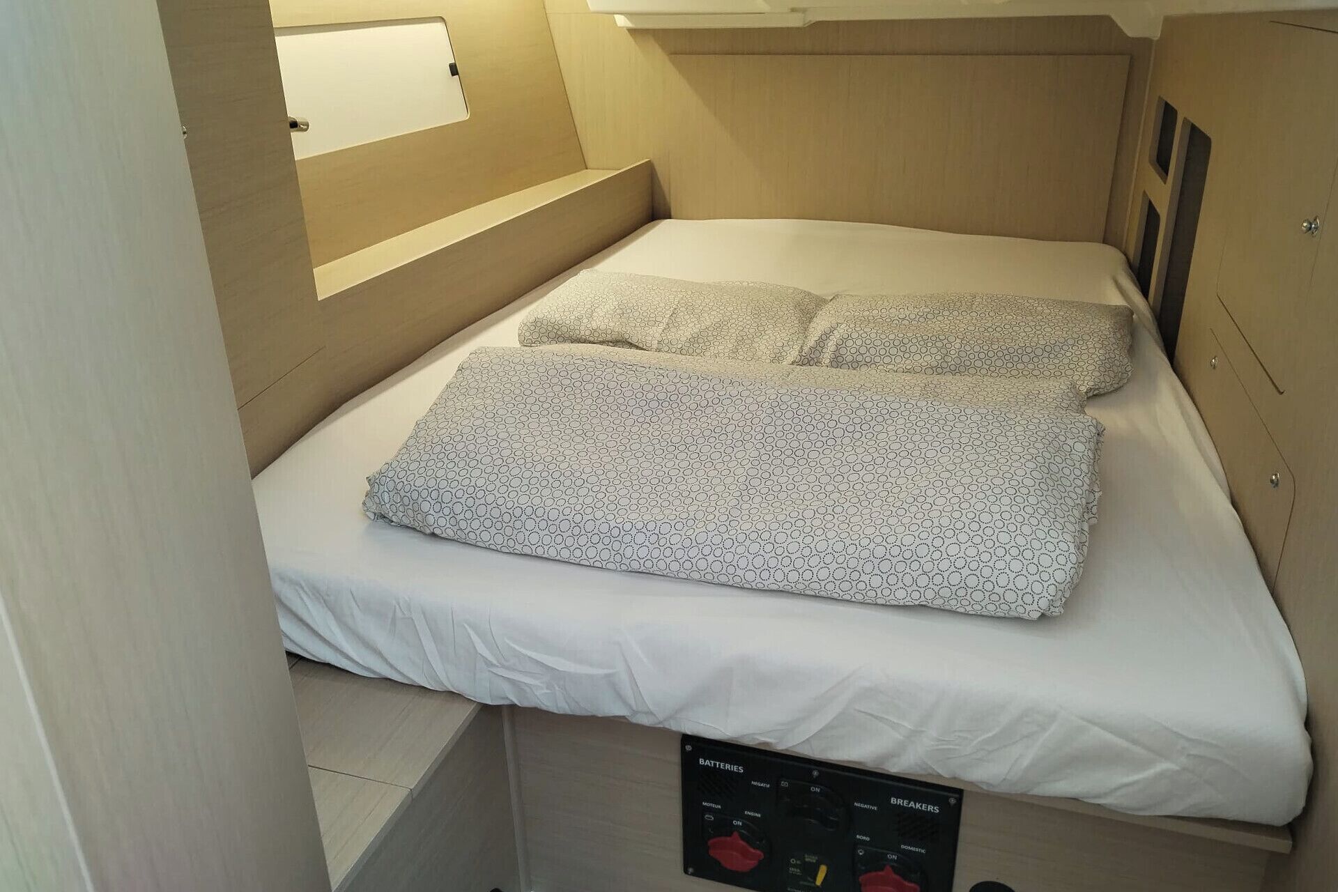 A compact room with a bed, a control panel, and a small window.