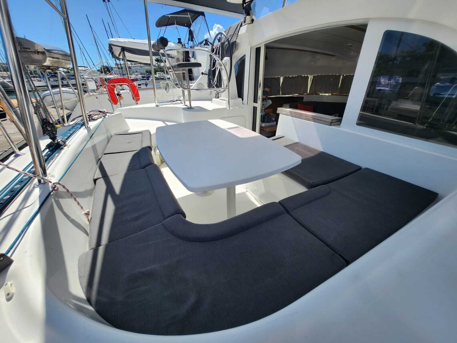 A boat's deck with a cushioned seating area, a table, and a steering wheel.