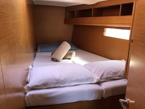 Habitació petita amb un llit búnquer de fusta, un finestral petit, roba de llit blanca i una tovallola arrotllada.