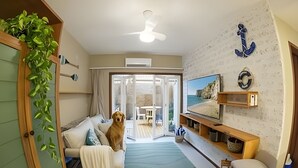 Ett vardagsrum med en soffa, en hund, en tv och utsikt över naturen.