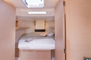 Ein kompakter, gut beleuchteter Raum mit Dachfenster, einem Bett mit Kissen und fest installierten Regalen.