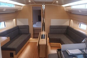 A compact interior with two seating areas, a central table, and a small bed. - Sun-Kissed Sailing Adventure in Northern Croatia (Punat)