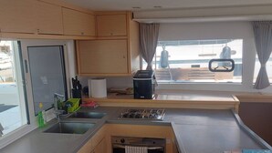 A compact kitchen with a sink, stove, and cabinets, a window with curtains, and a view of the outside. - Sun-Kissed Sailing Adventure in Split, Croatia (Split)
