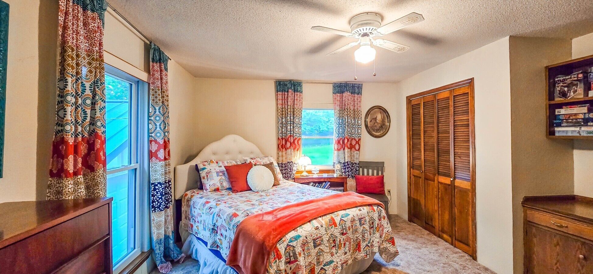 Ein Schlafzimmer mit Bett, Vorhängen, Deckenventilator, Fenster und Kleiderschrank.