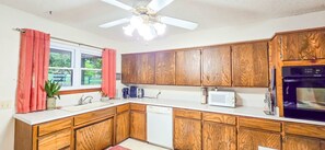 Una cocina con gabinetes de madera, microondas, lavavajillas y ventilador de techo.