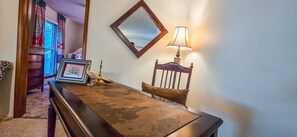 Una habitación con un escritorio de madera, una silla, una lámpara, un espejo y un cuadro en la pared.