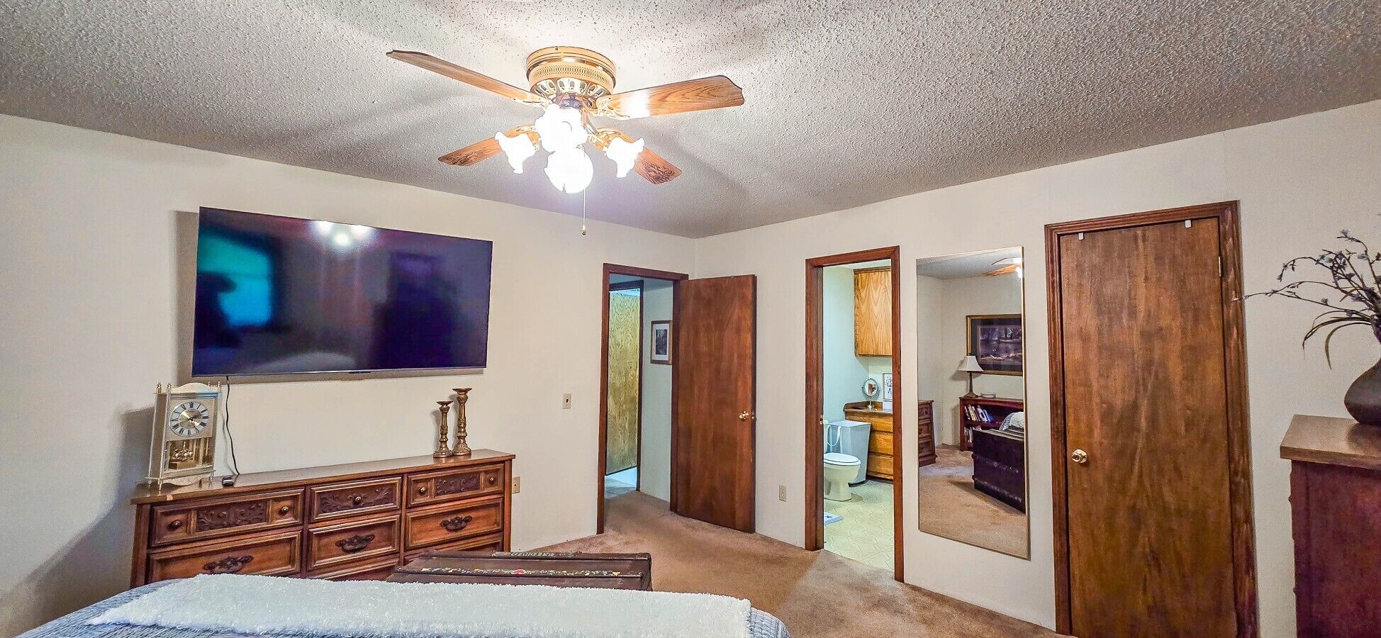A bedroom with a ceiling fan, a TV, a dresser, and a door leading to another room.