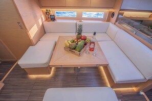 A boat interior with a wooden table, cushioned seating, and a view of the sea through windows. - Sun-Kissed Sailing Adventure in Islas Sarónicas (Alimos)