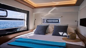 A bedroom with a bed, pillows, a hat, and a window with a view of the sea.