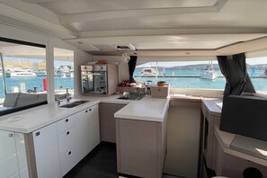 Een kleine kombuis met een spoelbak, fornuis en opbergkastjes, met uitzicht op een jachthaven met boten.