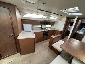 A compact kitchen with a refrigerator, stove, and sink, wooden cabinets, and a small dining area with benches. - Sun-Kissed Sailing Adventure in Zadar, Croatia (Biograd na moru)