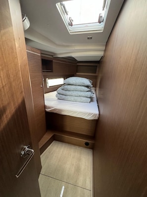 A compact RV interior with a skylight, a bed with patterned pillows, and wooden cabinetry.