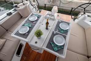 A boat's dining area with two tables, each set with plates, cutlery, and a bottle. - Sun-Kissed Sailing Adventure in the Ionian Islands, Lefkada (Lefkada)