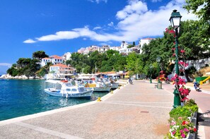 A coastal town with boats docked, a paved walkway, and buildings with red roofs.