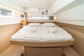 A bed with white linens and rolled towels, a wooden headboard, and a small window with curtains. - Sun-Kissed Sailing Adventure in Islas Esporadas (Skiathos)