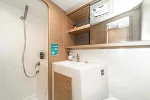 A compact bathroom with a shower, a sink, and a storage cabinet. - Sun-Kissed Sailing Adventure in Islas Esporadas (Skiathos)