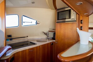 A compact kitchen with a sink, stove, and microwave, wooden cabinets, and a window.