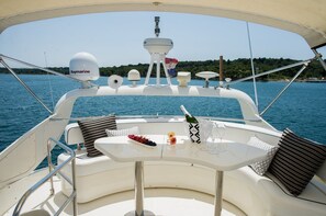 Ein Schiffsdeck mit einem Tisch für zwei Personen, einer Champagnerflasche und einer Obstschale.