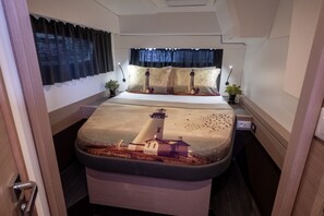Ein Schlafzimmer mit einem Bett mit Leuchtturm-Motiv, einem Nachttisch mit Lampe, einem Fenster mit Vorhängen und einer Tür.