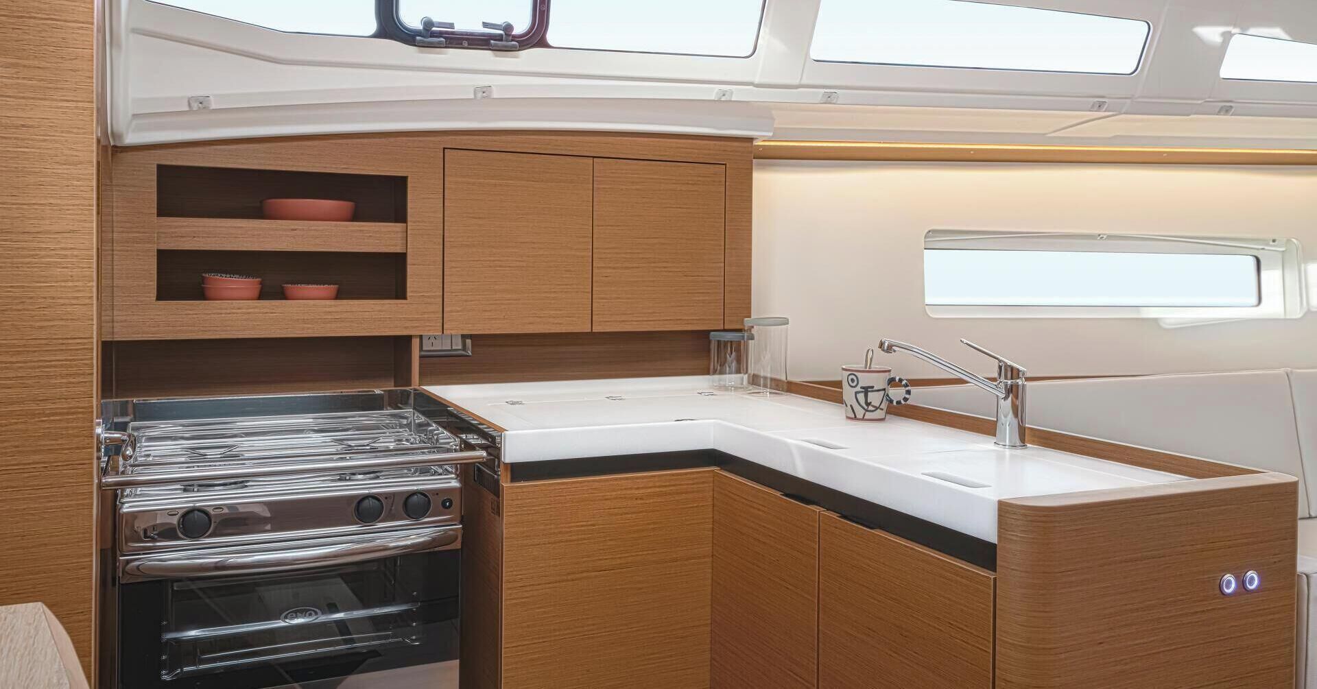 A compact galley kitchen with a stove, oven, and sink, wooden cabinets, and a window above the sink.