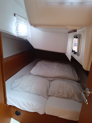 Ein kleines Bett mit Kopfteil, ein Fenster mit Vorhängen und eine kleine Deckenleuchte.